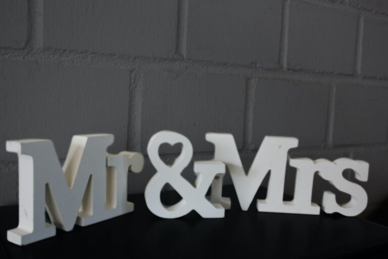Dekorative Buchstaben „Mr. & Mrs. Aufsteller“ vor einem grauen Ziegelwandhintergrund.