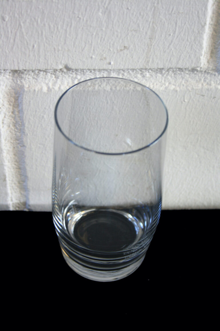 Ein leeres Wasserglas Mira steht auf einer schwarzen Oberfläche vor dem Hintergrund einer weißen strukturierten Ziegelwand.